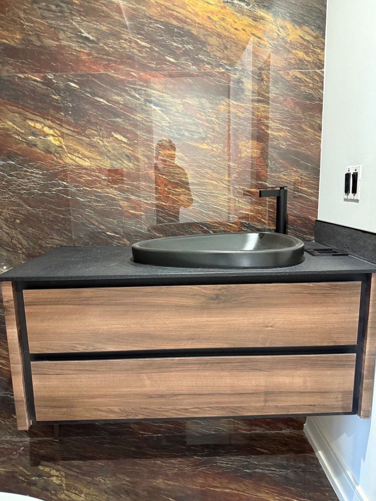 Custom wooden bathroom vanity with a black vessel sink and stone wall by KABCO